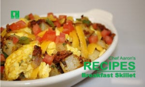 Breakfast skillet with eggs, potatoes, tomatoes, cheese, and peppers in a white dish